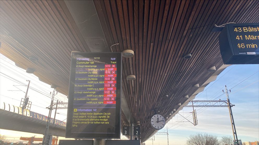 Tågstationens informationsskylt med avgångar, där flera tåg är markerade med röd kryss, vilket indikerar inställda avgångar. Till höger syns en klocka och en digital nedräkning för nästa tåg till Bålsta, med information om väntetid.