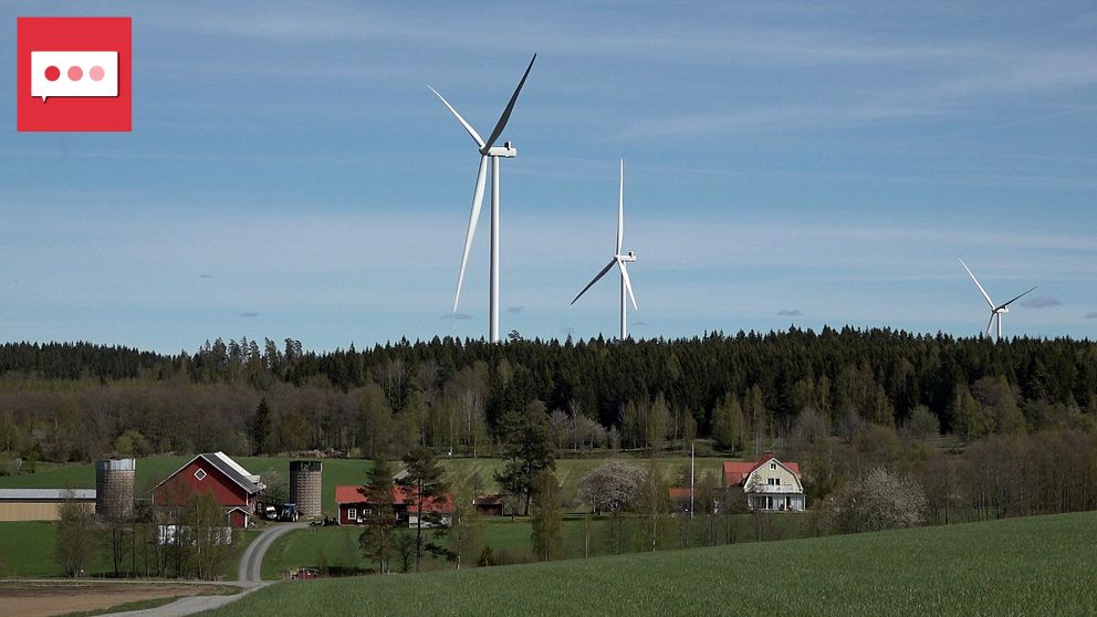 Flera vindkraftverk bakom gårdar och åkermark i lantlig miljö.