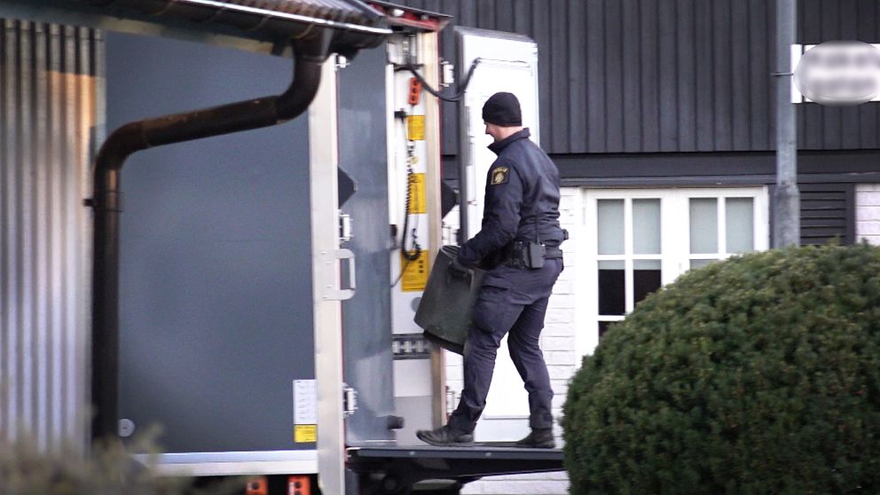 En polis från Nationella bombskyddet bär en tunna och går in i en lastbil vid en byggnad, omgiven av grönska.