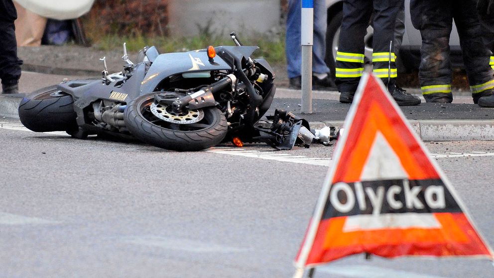 Omkullvält motorcykel, olycksvarningstriangel i förgrunden, brandmän i bakgrunden.