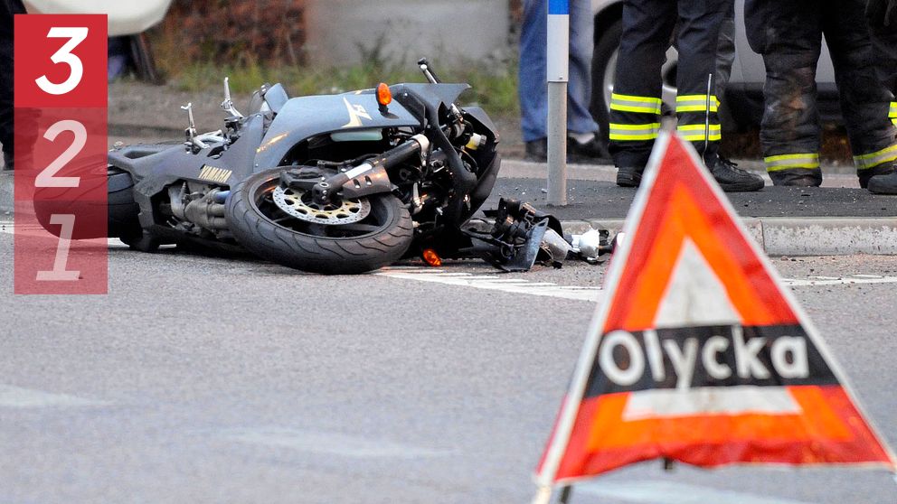 Omkullvält motorcykel, olycksvarningstriangel i förgrunden, brandmän i bakgrunden.