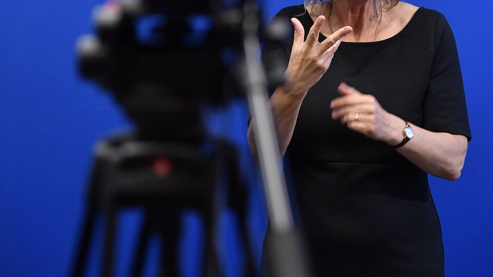 Teckenspråkstolk gestikulerar framför kamera i studio.