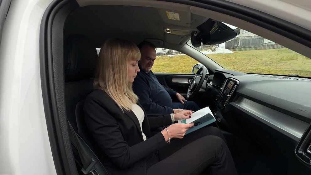 Två personer sitter i en bil och läser en bok.