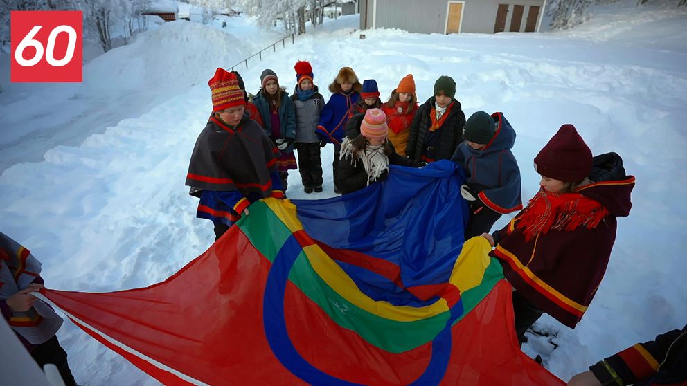 Grupp samer håller upp en samisk flagga i ett snötäckt landskap.