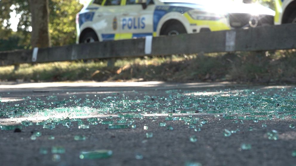 Glas på marken efter en skjutning i Årby. En polisbil står i bakgrunden.