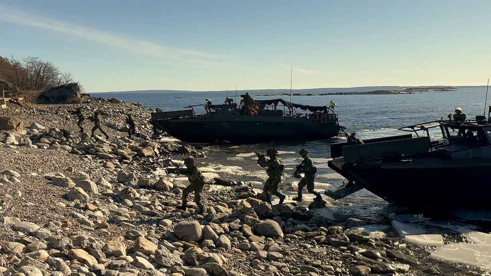 Soldater stiger i land från militärbåtar vid stenig kust.