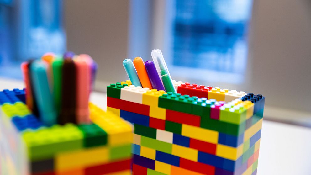 Färgglada pennhållare byggda av legobitar med pennor i, under ett fönster.