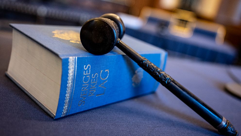 En blå bok ”Sveriges rikes lag” på ett bord. En domarklubba ligger ovanpå.