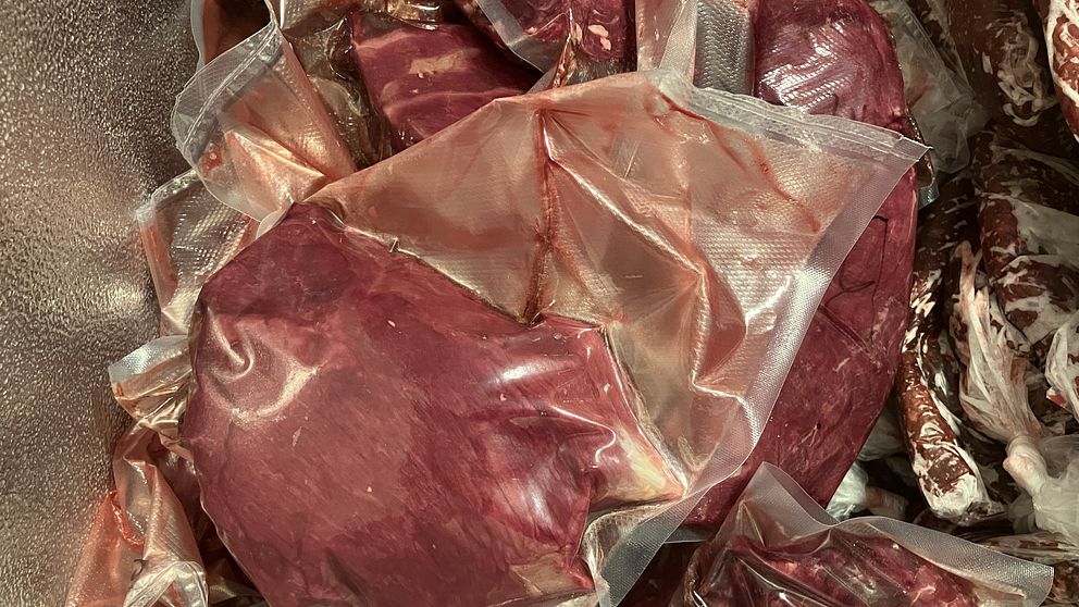 Förpackat kött i vakuumförpackningar, staplat i en frys eller kyl. Köttet har en mörkröd färg och är synligt i flera olika förpackningar.
