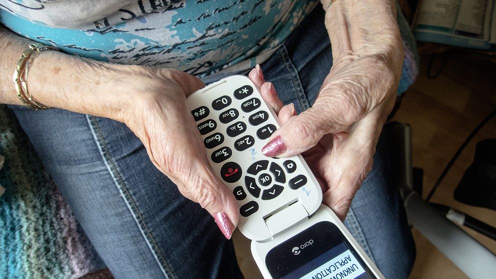 Äldre kvinna håller i en knapptelefon.