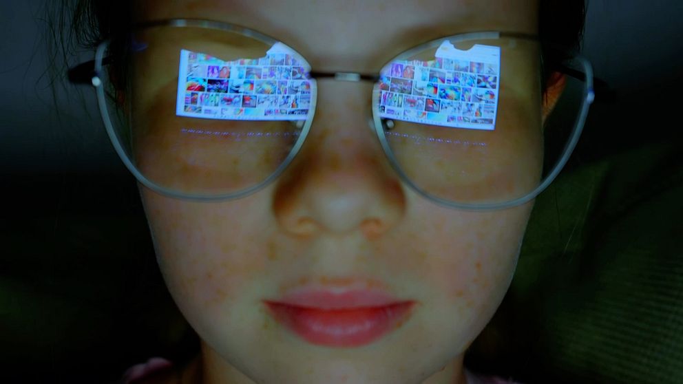 Närbild flicka med glasögon där bildskärm med foton från sociala medier speglas.