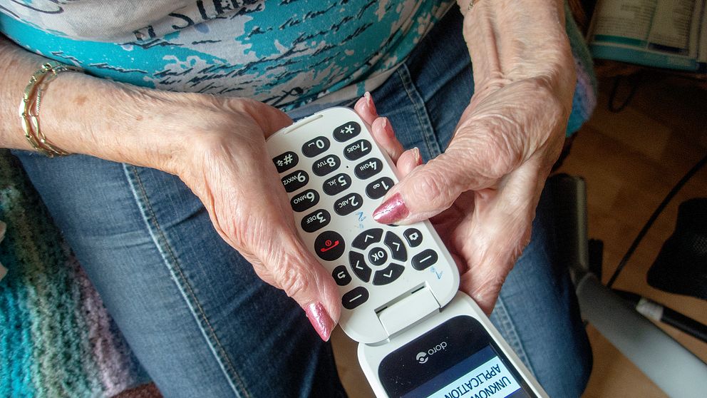 En äldre person håller i en mobiltelefon med stora knappar, medan en annan, mindre telefon visas i bildens nedre del.