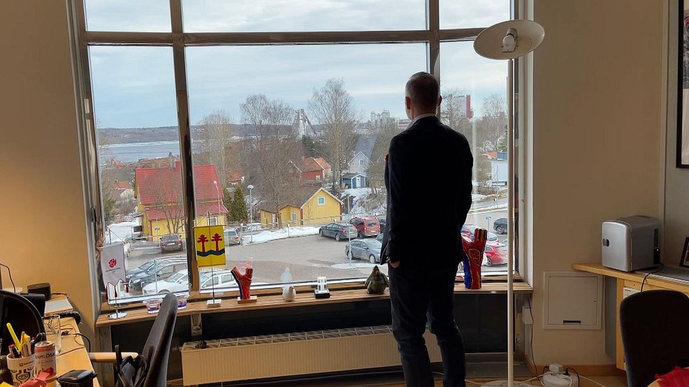 Person står vid fönster och blickar ut över snöigt stadslandskap.
