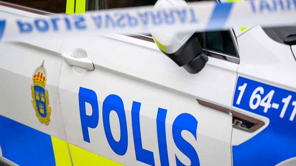 En polisbil med tydlig märkning och avspärrningsband i fokus.