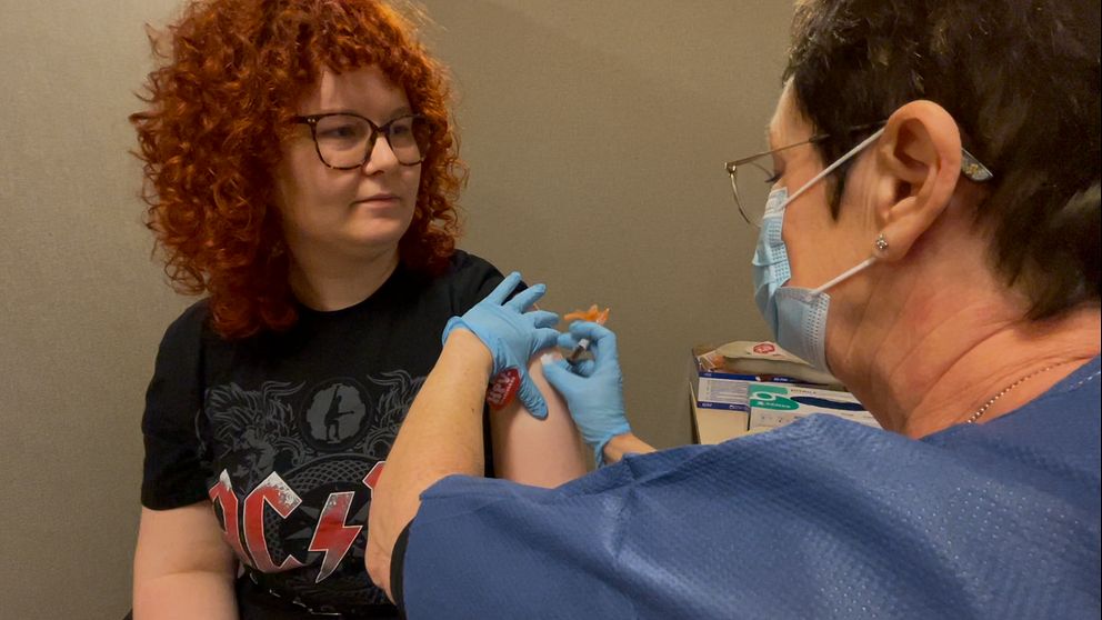En ung kvinna får sin vaccinspruta av en sjuksköterska med munskydd
