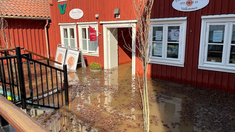 Rött hus omgärdat av översvämmat vatten, trottoar delvis under vatten.
