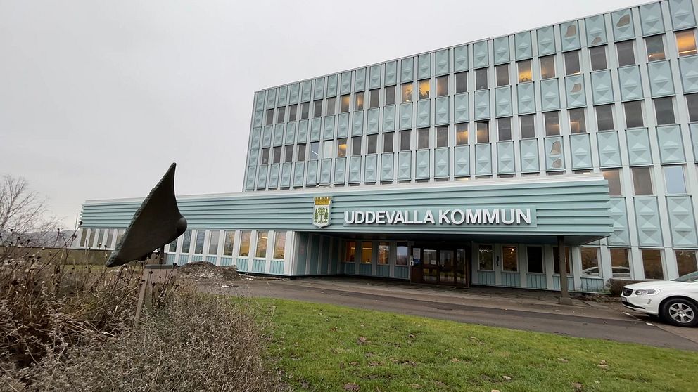 Byggnaden som rymmer Uddevalla kommun, en modern kontorsbyggnad med stora fönster och en ljusblå fasad. Framsidan har en tydlig skylt med texten ”UDDEVALLA KOMMUN”, och en skulptur i förgrunden.