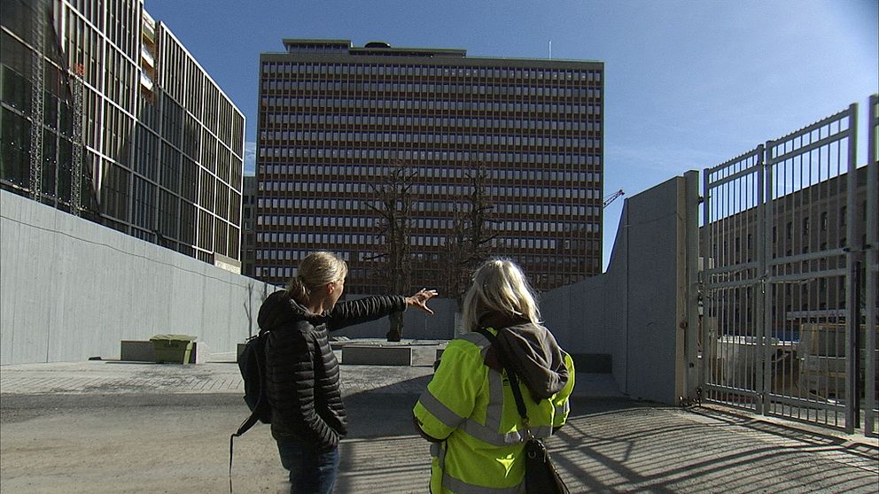 Två personer diskuterar framför ett stort kontorshus under en klarblå himmel.