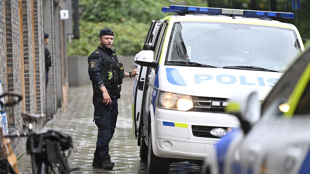 Polis står utanför en polisbil på en gata på Södermalm i Stockholm.
