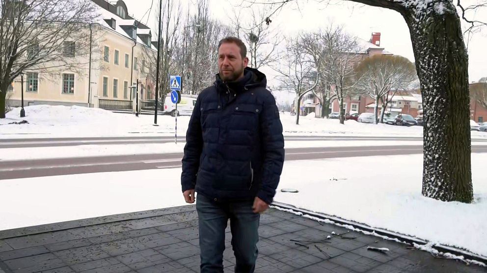 en skolchef som går på en gata med hus bakom , snömiljö runtom.