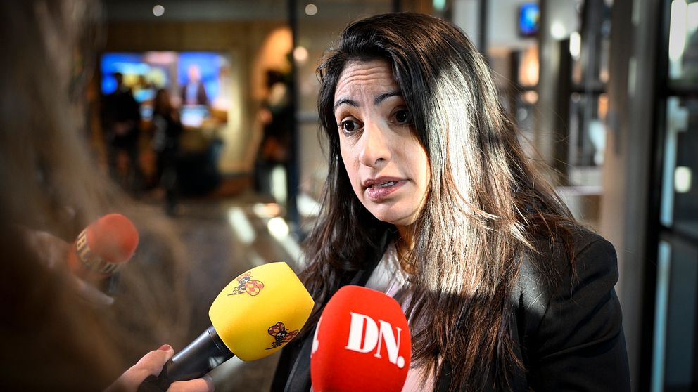 Person intervjuas av flera reportrar med mikrofoner från SVT och DN i en offentlig miljö.