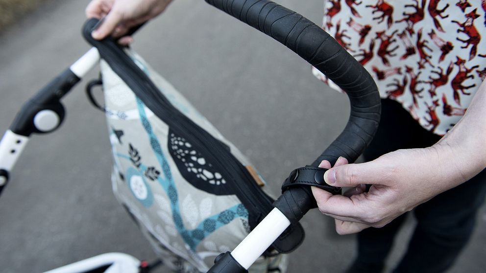 Händer på upphängningsanordning för skötväska för barnvagn.