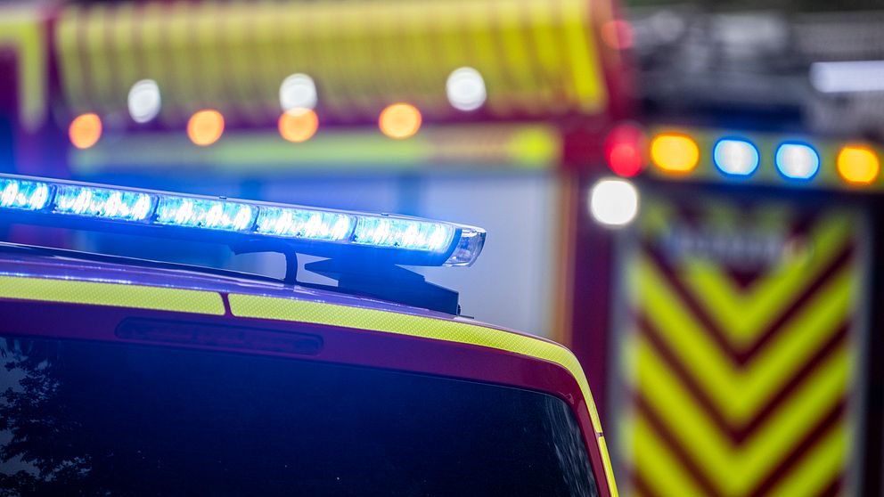 Brandbilar med blåljus aktiverade, fokuserad del visar taket på en utryckningsfordon och en annan brandbil syns i bakgrunden.