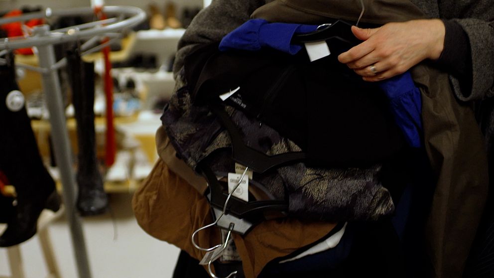 Person bär på flera jackor i en butik.