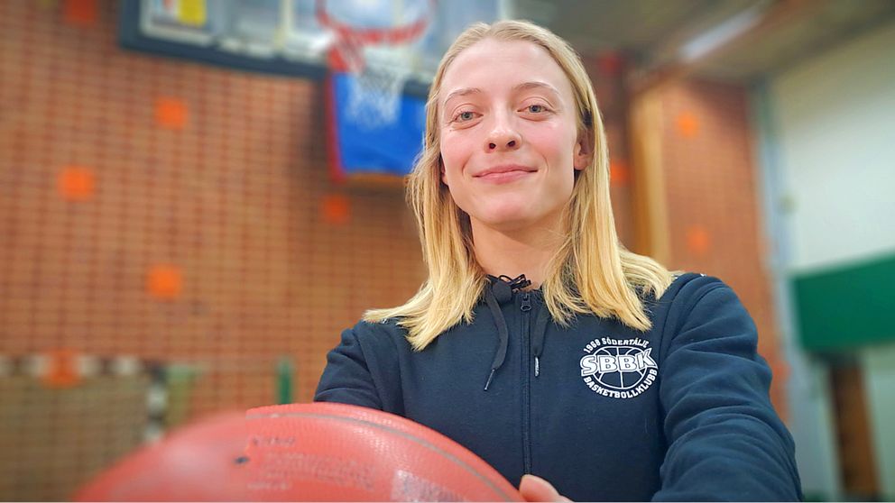 Basketspelaren Klara Lundquist håller i en basketboll framför kroppen med korg i bakgrunden
