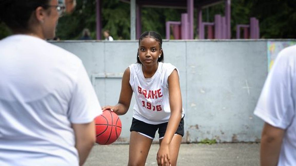 Ung kvinna dribblar en basketboll på en utomhusplan.