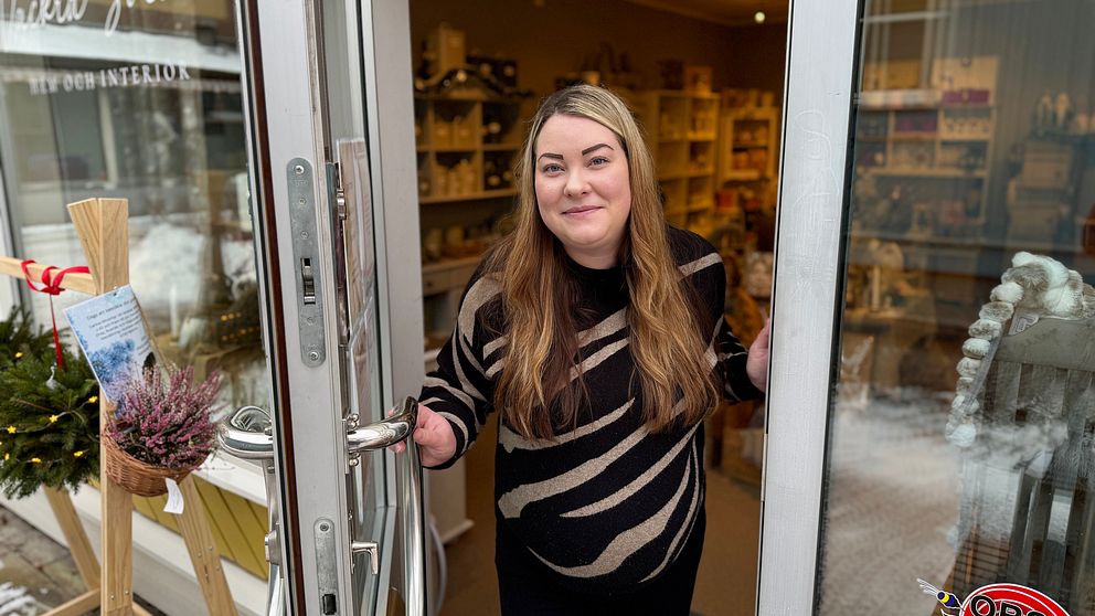 Jessika Skarin står vid ingången till sin butik i Orsa. Butiken är en presentbutik med inredning och presentartiklar. Det är vinter och snö syns på marken utanför.