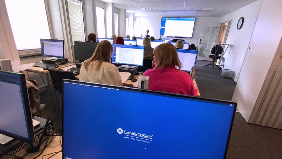 I ett kontorsutrymme sitter flera personer vid sina datorer och deltar i en presentation.