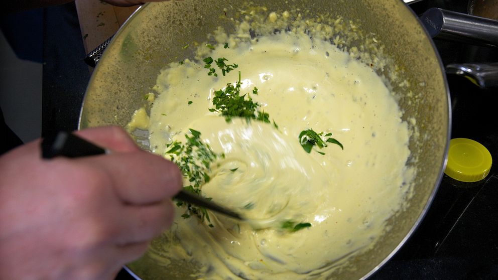 Någon vispar ihop en krämig sås med hackad persilja i en stor skål.