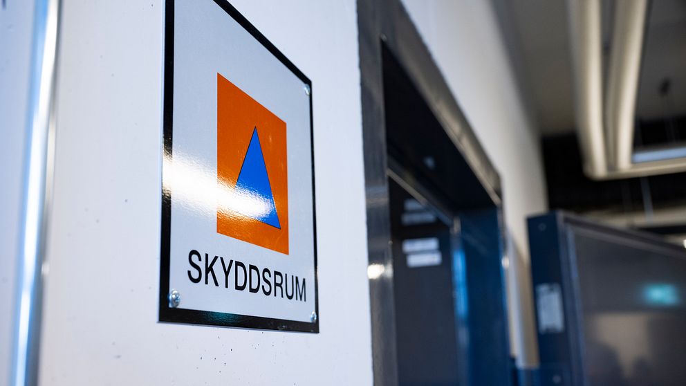 Skyddsrummets skylt med orange och blå symbol på en vit vägg, som tydligt anger platsen för skyddsrummet.