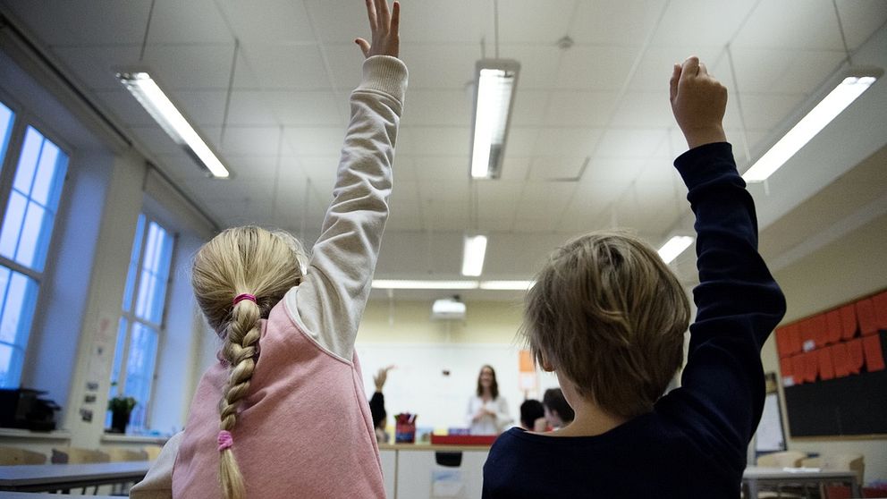 Barn i klassrum räcker upp handen.