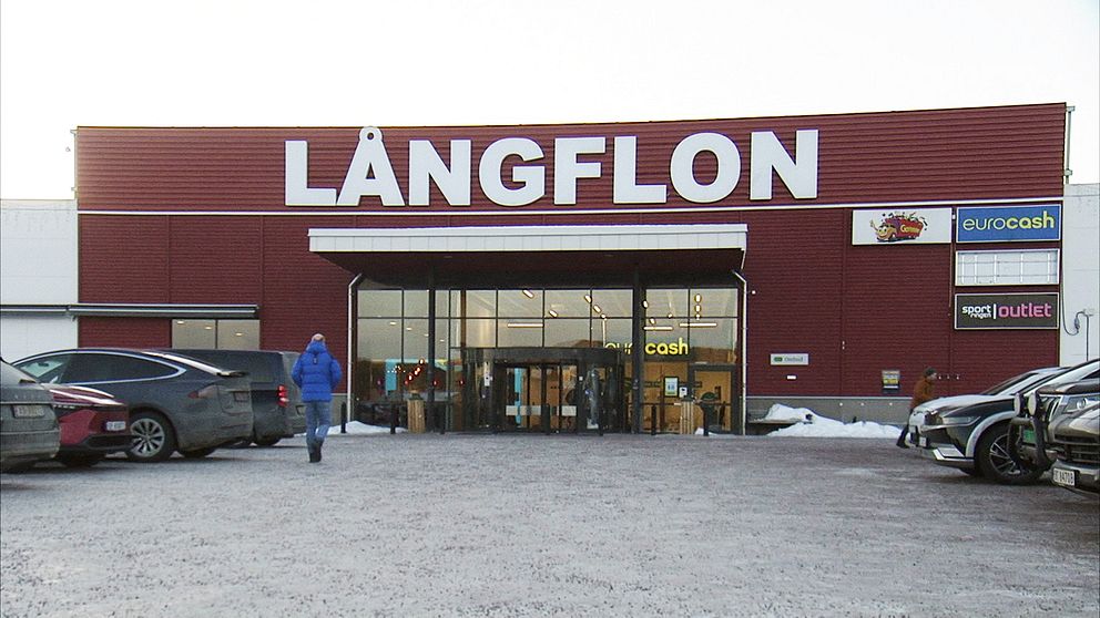 Ingången till köpcentret Långflon, med parkerade bilar och en person som går mot dörren.
