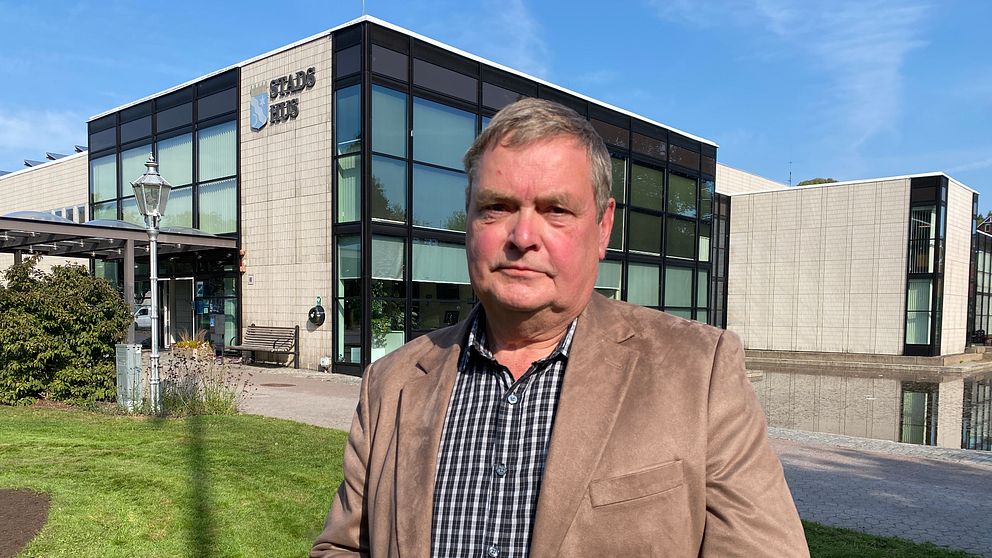 En person står framför en modern byggnad med stora fönster, där skylten ”Stadshus” är synlig. Byggnaden omges av grönska och det är klar himmel. Hyresgäst, hyresvärd, hyresrätter.