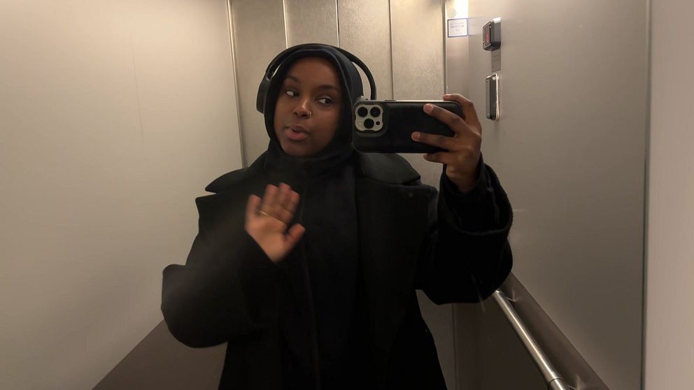 En ung kvinna filmar sig själv med mobilen genom en hisspegel.