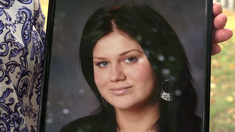 En person håller ett porträttfoto med mörkhårig kvinna i svart klädsel och örhänge.