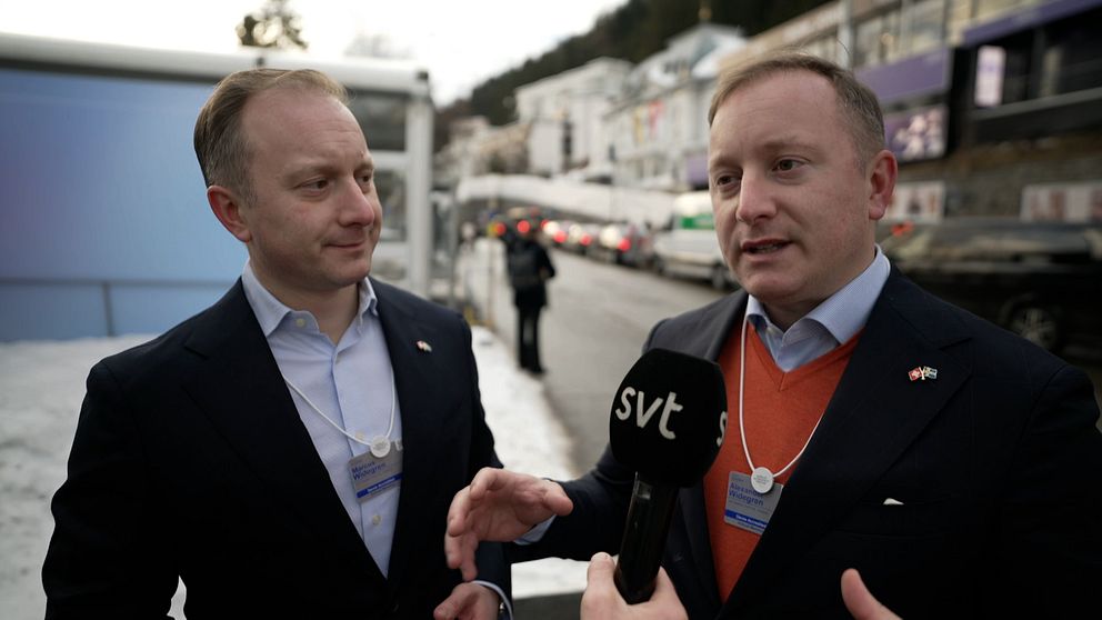 Två män i affärskläder står utomhus och diskuterar medan en person med en mikrofon, som representerar SVT, intervjuar dem. Bakgrunden visar snötäckta gator och byggnader.