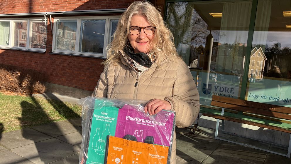 En kvinna i ljus jacka som håller i ett kit med skräpsorteringspåsar.-
