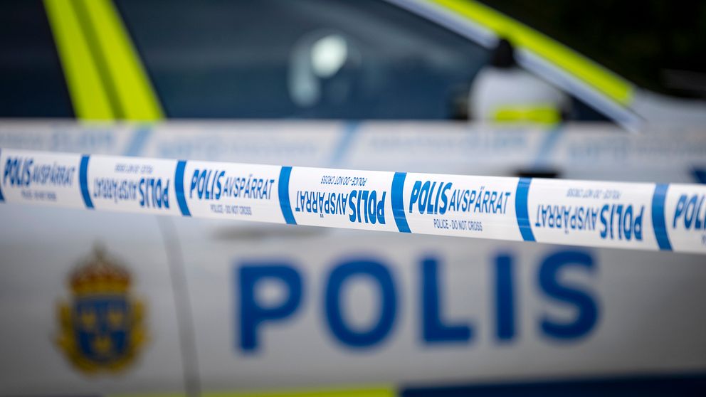 En avspärrning med polisband i förgrunden, med en svensk polisbil synlig i bakgrunden. Bandet har texten ”POLIS AVSPÄRRAT”.
