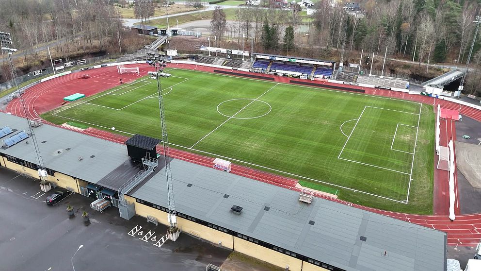 En översiktlig bild av Finnvedsvallen i Värnamo med gräs och löparbana. I förgrunden syns en byggnad med flera takfötter, och det finns två fotbollsmål på planen. Bakom planen finns läktare och träd. Bilden är tagen från luften, vilket ger en komplett vy av området.
