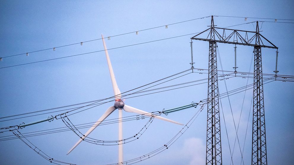 Vindkraftverk och kraftledningar mot blå himmel.