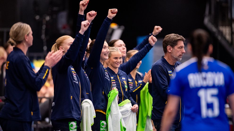 Glada handbollsspelare på bänken firar med knutna nävar under matchen.