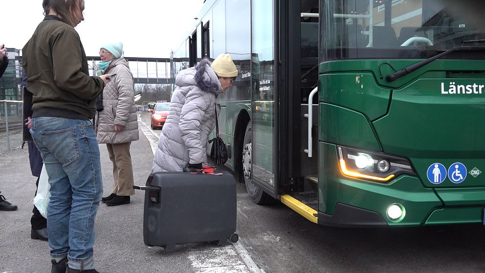 Kvinna med resväska på väg in i buss.