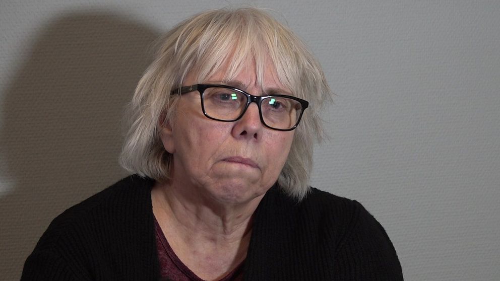 Kvinna med vitt hår som sitter mot en grå vägg