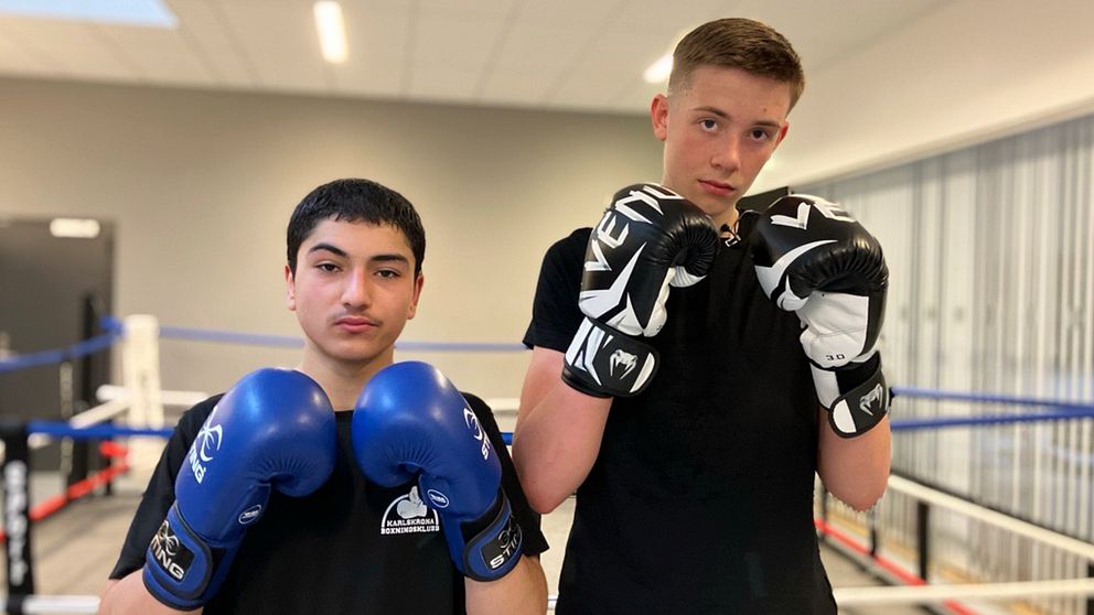Två personer i boxningshandskar poserar i en boxningsring inomhus.