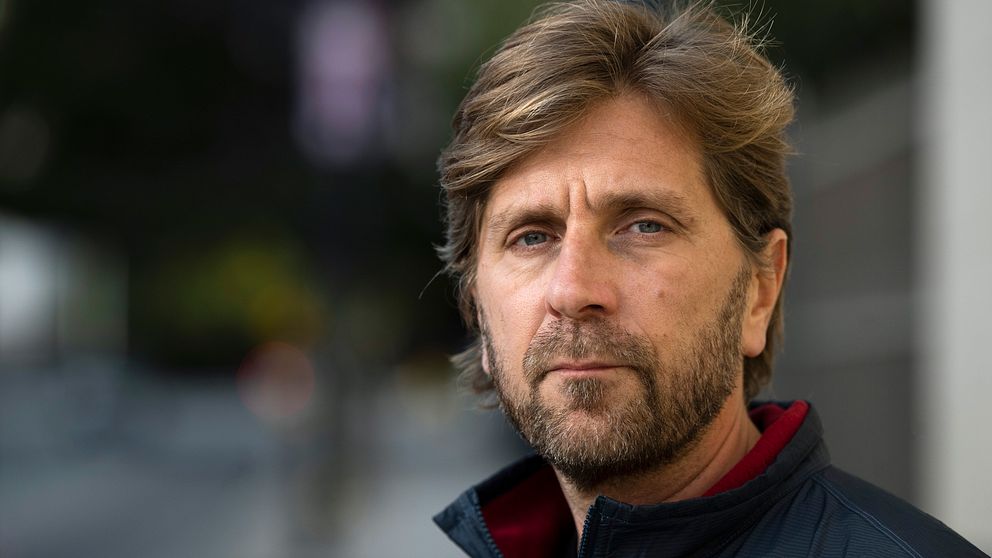 Ruben Östlund i en mörk jacka står utomhus med en oskarp stadsbakgrund.