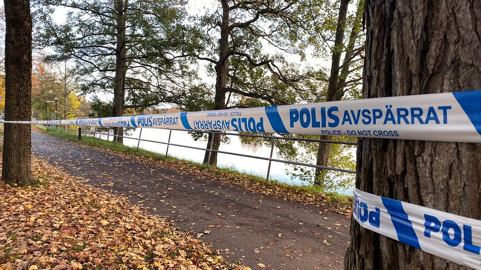 Avspärrad väg vid en sjö. Blått polisavspärrningsband sträcker sig längs med vägen.
